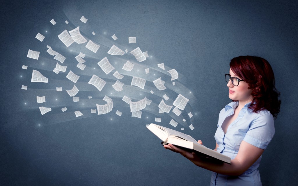 "A young woman with red hair and glasses, wearing a light blue shirt, is holding an open book. Pages from the book appear to be magically floating and dispersing into the air, creating a sense of imagination and knowledge."